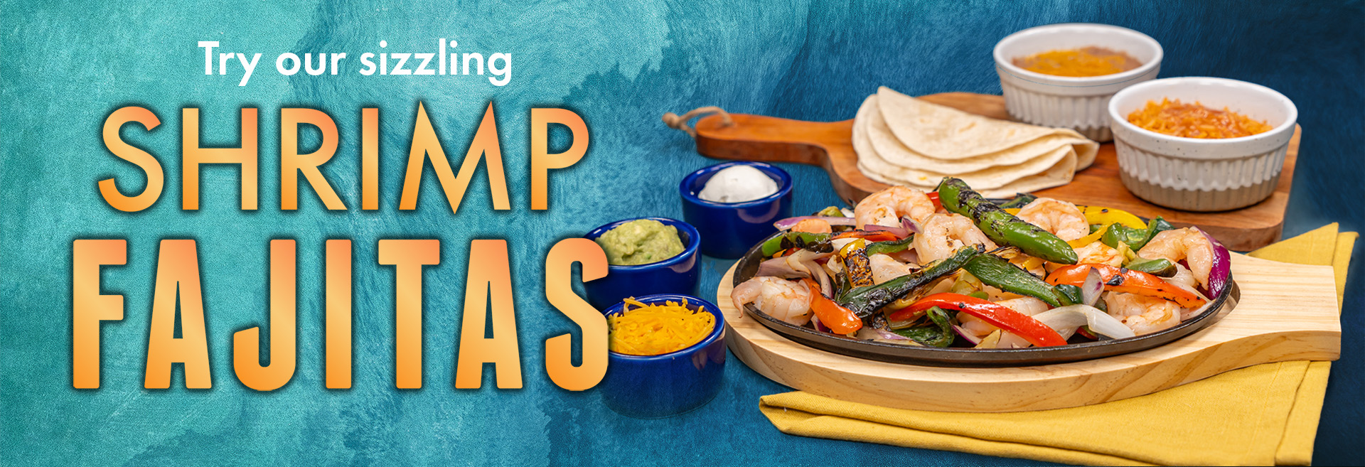 The image displays a vibrant and colorful serving of shrimp fajitas with the inviting text "Try our sizzling SHRIMP FAJITAS" placed above. The fajitas are presented on a skillet with shrimp and assorted grilled vegetables. Accompanying the main dish are sides of shredded cheese, sour cream, guacamole, and rice, with tortillas on the side, all laid out on a wooden board over a blue textured background. The image is likely intended for use as an advertisement or menu promotion.